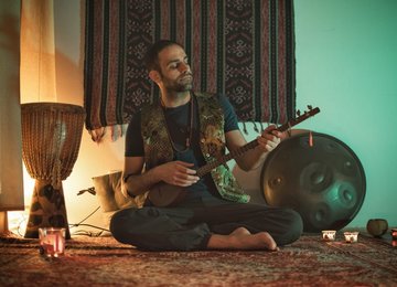 Morteza Ketabnevis spielt Sitar am Boden sitzend, neben ihm eine Handpan und eine Djembe